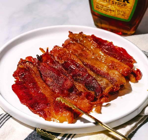 Plate of candied bacon with a bottle of maple syrup in the background.